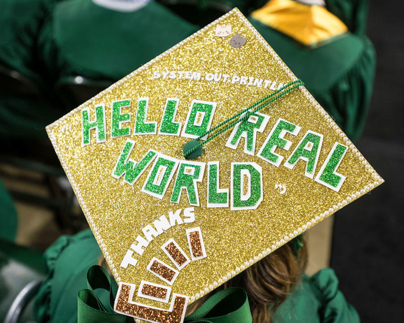 George Mason University graduate's mortarboard cap decorated with the phrase "Hello Real World" in block letters and gold glitter