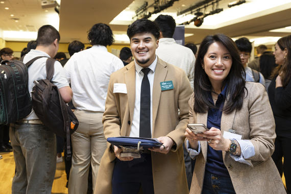 Two individuals smiling during the Spring Career Fair 2024, standing in a professional setting surrounded by other attendees