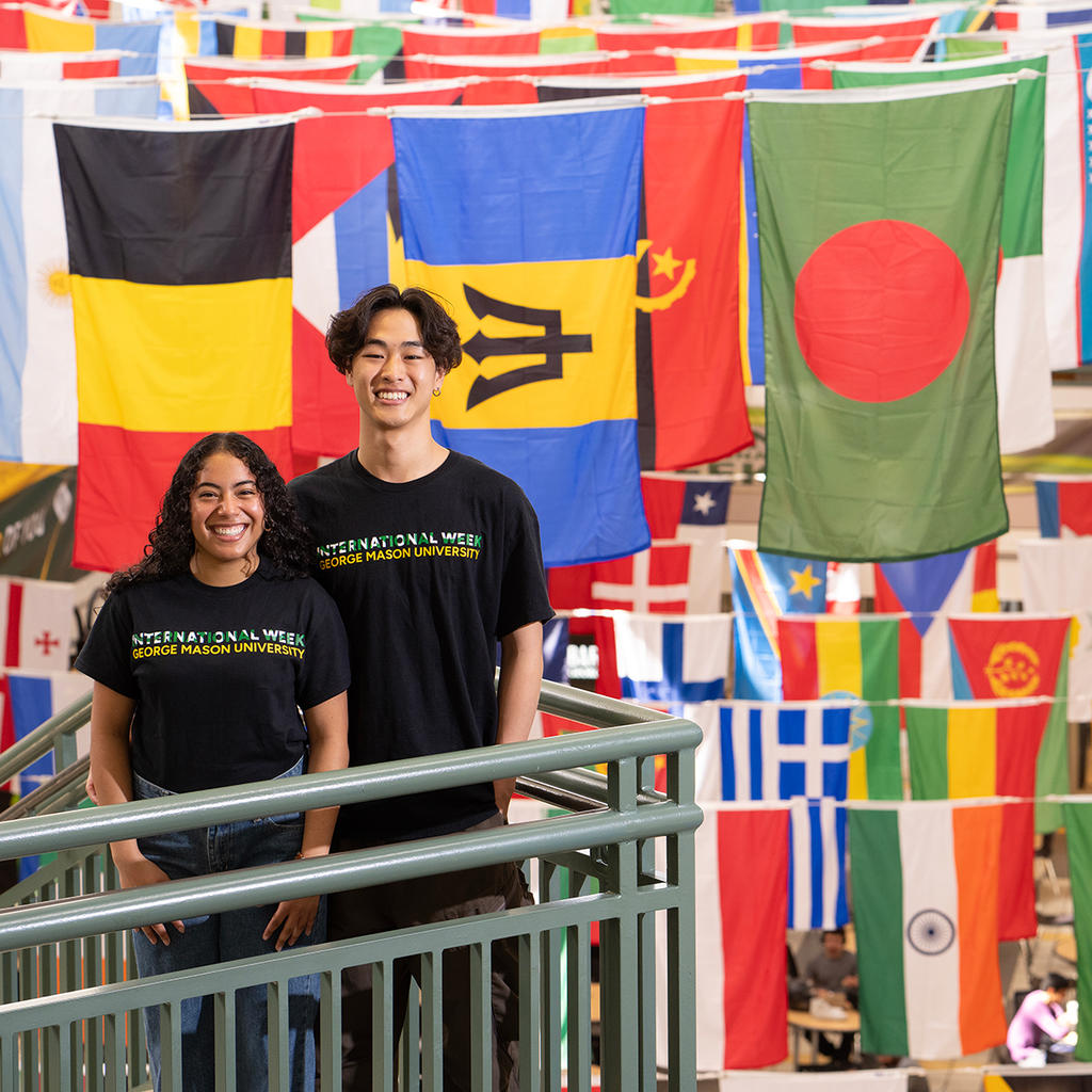 Two students celebrate International Week at George Mason University, surrounded by colorful world flags