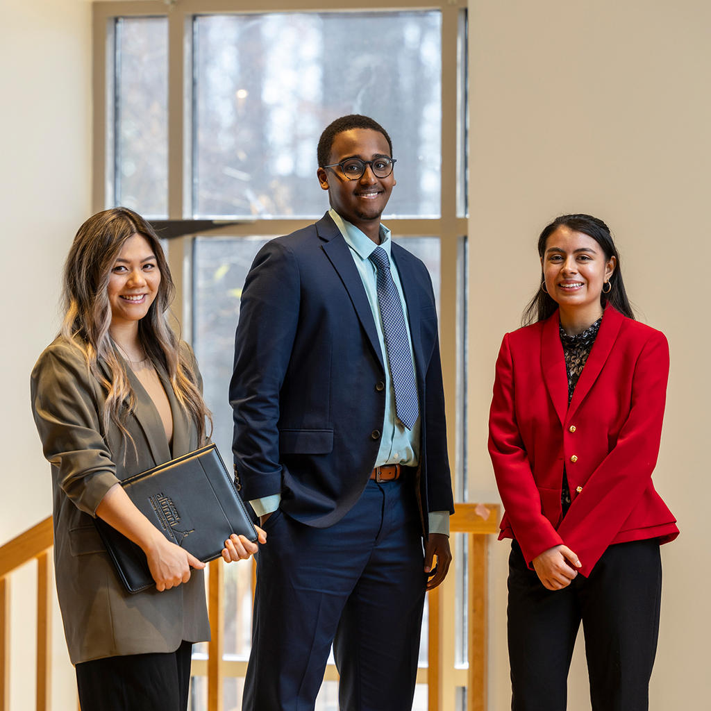 Three students in professional attire pose confidently indoors, preparing for career opportunities.